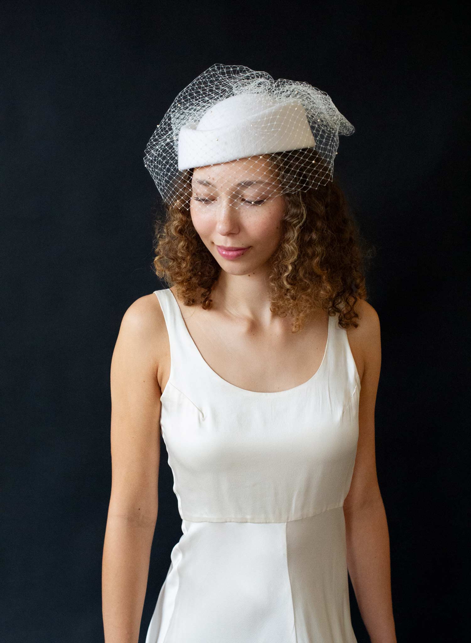 Bridal pillbox hat with pearl adorned birdcage veil and bow